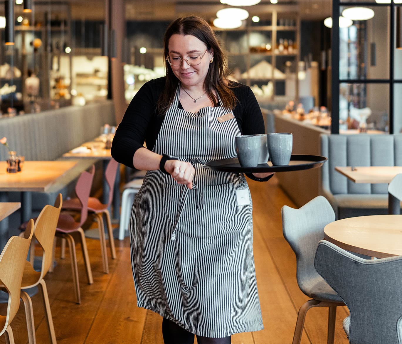 Bild eines Kellners, der mit einem Teller mit drei Tassen Kaffee auf seine Solar-Pager-Uhr schaut