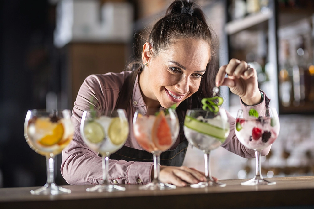 Kellnerin richtet fünf farbenfrohe Cocktails im Restaurant an – Fokus auf Service und Gastfreundschaft.